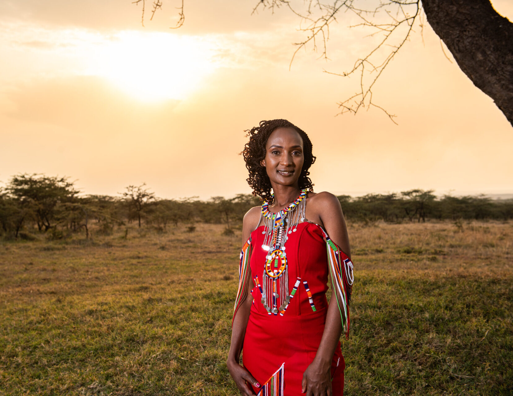 Woman in red dress standing in the Maasai Mara savannah at sunset.